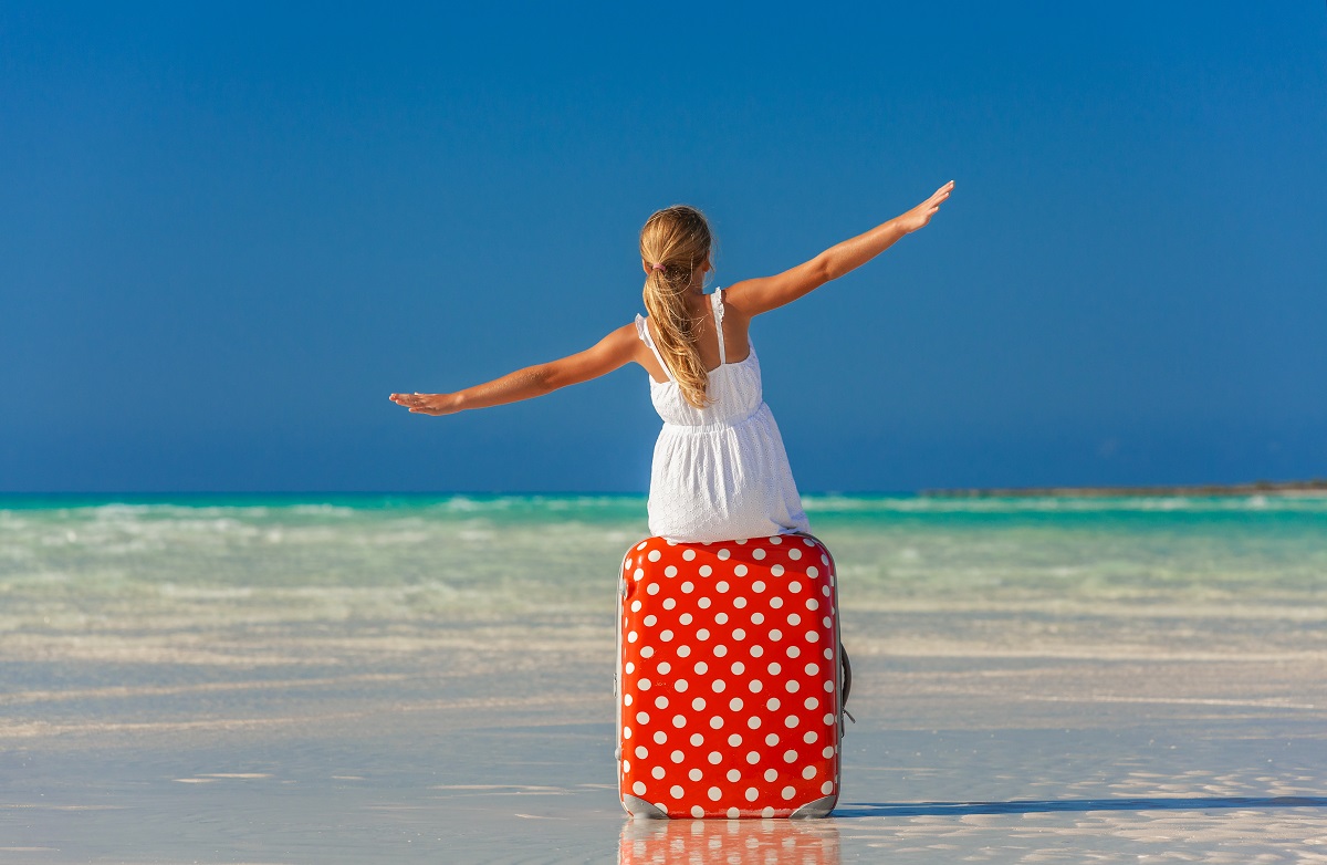 Luxury travel on a budget - girl sitting on a polka dot luggage looking at the sea