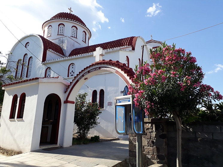 Greek white church on Samothraki with red brick roofs and a pink oleander in front.